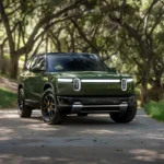 Rivian R2 Forest Green parked on a tree-lined road, front three-quarter view