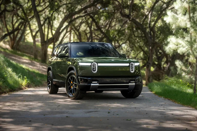 Rivian R2 Forest Green parked on a tree-lined road, front three-quarter view