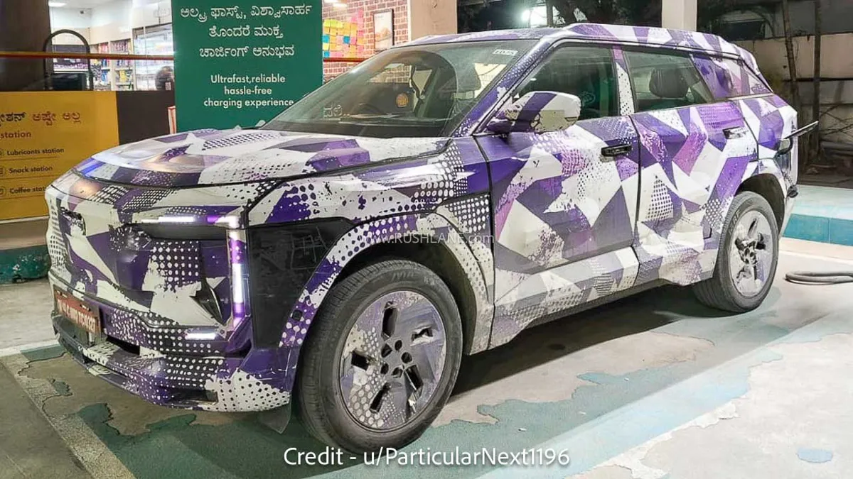 Camouflaged Mahindra BE 7 test mule in white and violet wrap at a Shell charging station in Karnataka, front three-quarter view