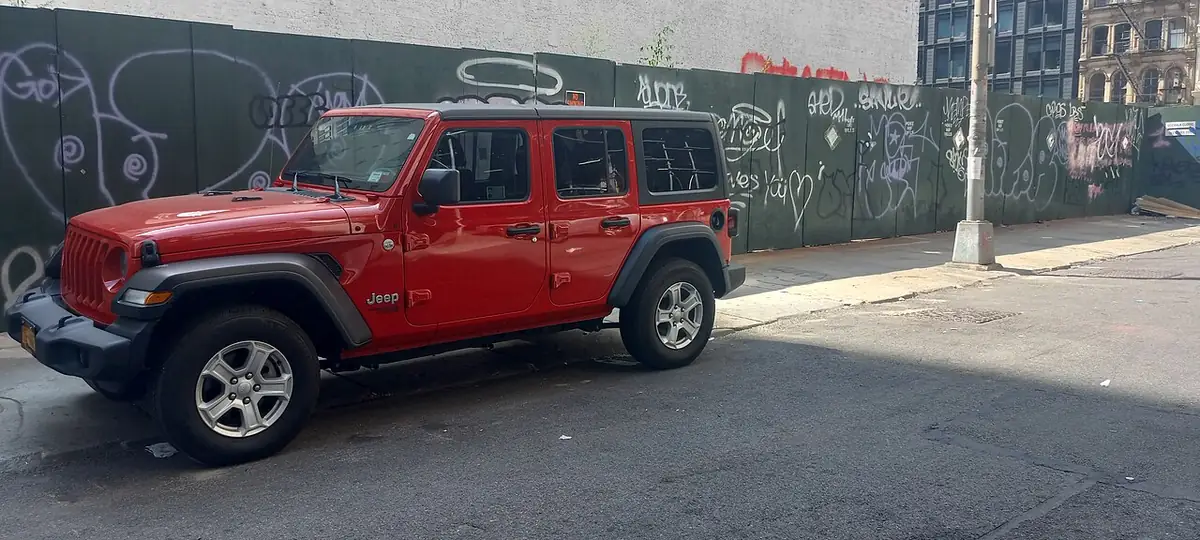 Red Jeep Wrangler Unlimited parked on a city street; red is now a paid option among 2027 Jeep Wrangler colors on the base Sport