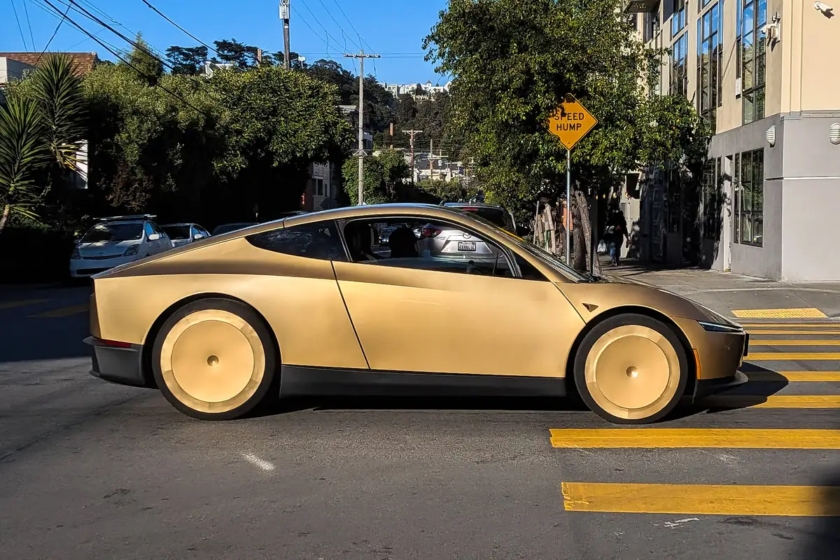 Gold Tesla Cybercab driving on a city street, the same type of car now expected for Tesla Robotaxi in San Antonio