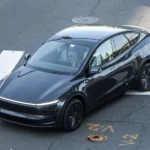 Dark gray refreshed Tesla Model Y driving through an intersection, seen from above; owners report Tesla V2L adapters broke after a software update
