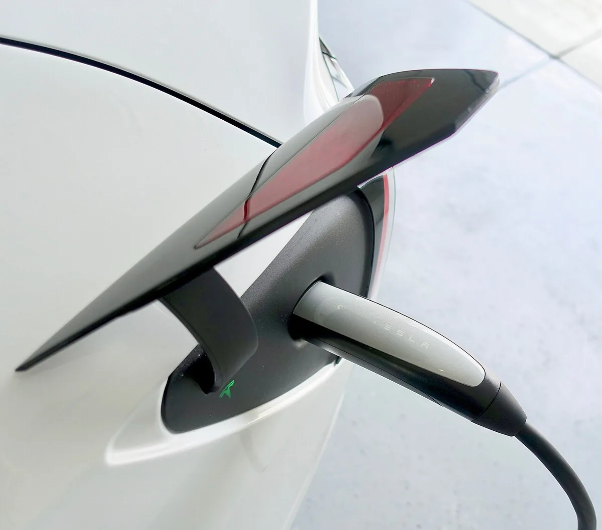 Close-up of a charging cable plugged into the charge port of a white Tesla Model 3, the port third-party Tesla V2L adapters use